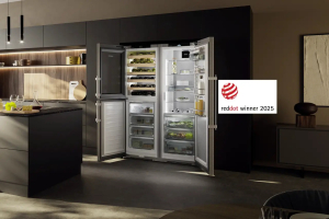 Modern kitchen with an open, illuminated Liebherr’s Premium BioFresh fridge displaying neatly organised food items. Sleek design with a Red Dot Award 2025 badge on the side.