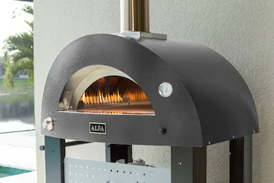 A sleek, outdoor pizza oven with a curved, black exterior stands against a wall. Inside, bright flames flicker warmly, evoking a cozy and inviting atmosphere.